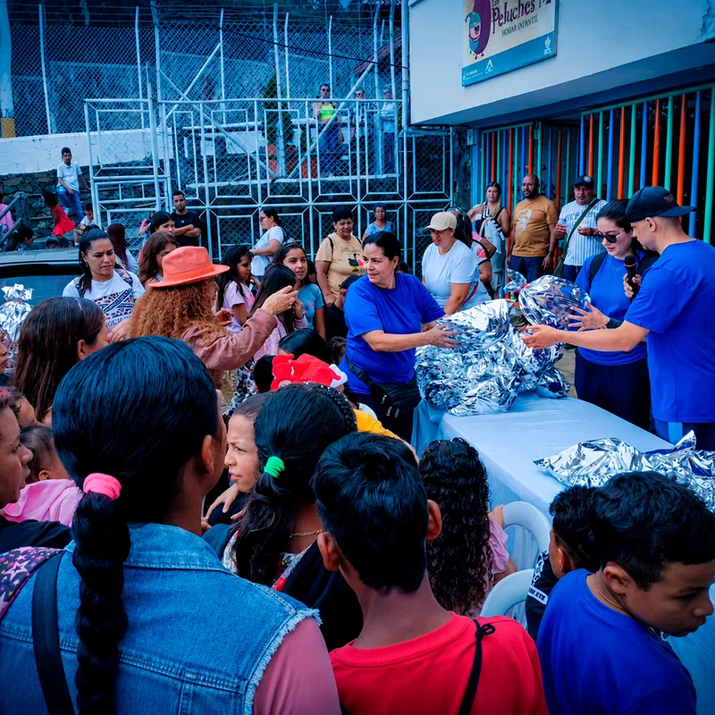 Voluntarios entregando regalos plateados a familias frente al Hogar Los Peluches.