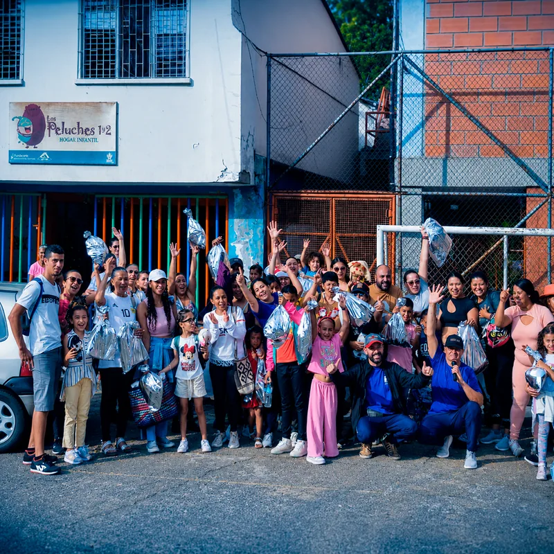Grupo grande frente al Hogar Infantil Los Peluches celebrando con los regalos en alto.