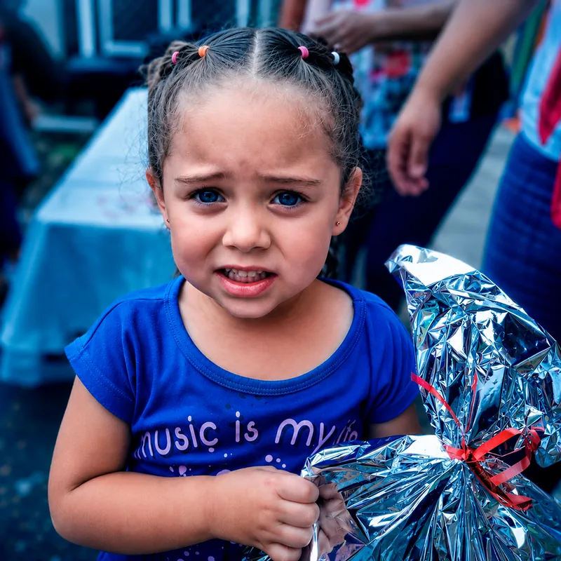 Niña con dos coletas sosteniendo un regalo plateado con lazo rojo.